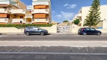 Asuinkatu, jonka varrella on parkkeerattuina kaksi autoa, portilla varustettu sisäänkäynti ja rakennus, jossa on parvekkeita ja puu.