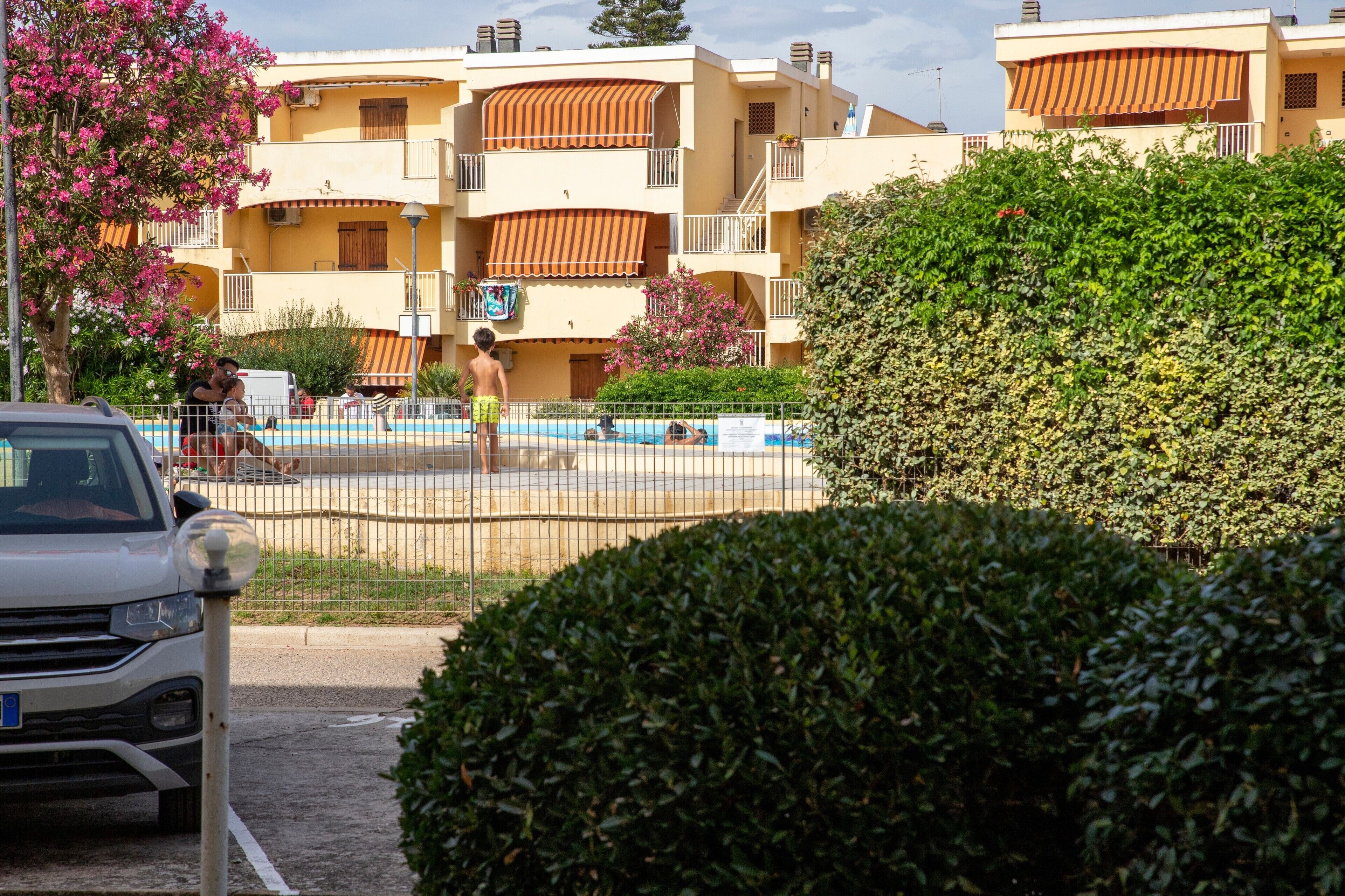 Un edificio residencial con balcones, una piscina y un coche estacionado.
