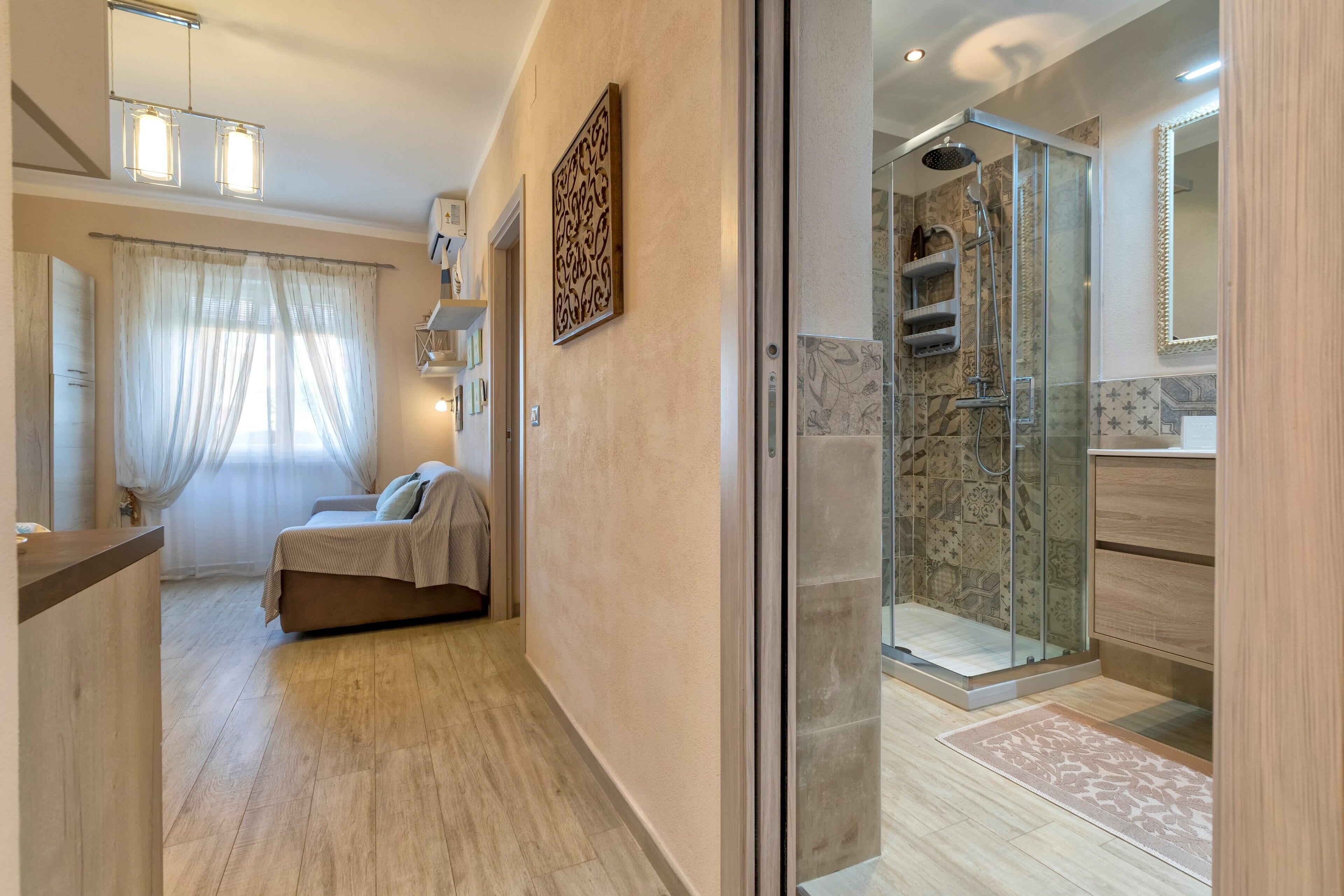 Een hotelkamer met een bed, een badkamer met een douchecabine van glas, en een gang met een spiegel en een deur.