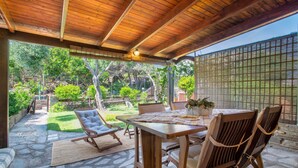 An outdoor patio with a wooden table, chairs, and a cushioned chair. - Holiday Home 'Stintino La Pelosa' with Private Terrace, Wi-Fi and Air Conditioning (Stintino)