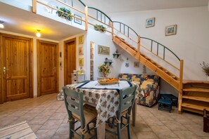 Comedor con una mesa dispuesta para dos, una escalera de madera y un sofá.