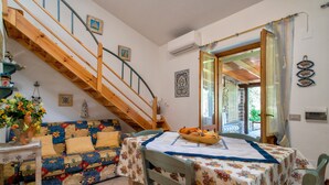 A cozy room with a wooden staircase, a dining table with a floral tablecloth, and a sofa with a colorful quilt. - Holiday Home 'Stintino La Pelosa' with Private Terrace, Wi-Fi and Air Conditioning (Stintino)