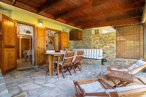 A stone-floored patio with wooden furniture, a dining table, and a staircase leading to an upper level.