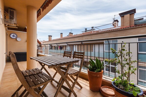 Un balcon avec une table et des chaises en bois, des plantes en pot et une vue sur les bâtiments voisins.