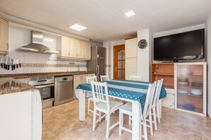 A kitchen with white cabinets, a stainless steel range hood, a refrigerator, a dishwasher, and a dining table with chairs.