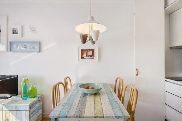 Un coin repas comprenant une table, des chaises, un bol de noix, un luminaire suspendu et des tableaux encadrés accrochés au mur.