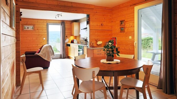 Un intérieur en bois comprenant un coin repas, un canapé et une vue à travers une porte vitrée.