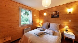 Une pièce aux murs lambrés, comprenant un lit, deux tables de chevet avec des lampes, une fenêtre avec des rideaux et un tableau accroché au mur.