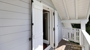 Une véranda couverte avec une balustrade blanche, une porte coulissante et une terrasse en bois.