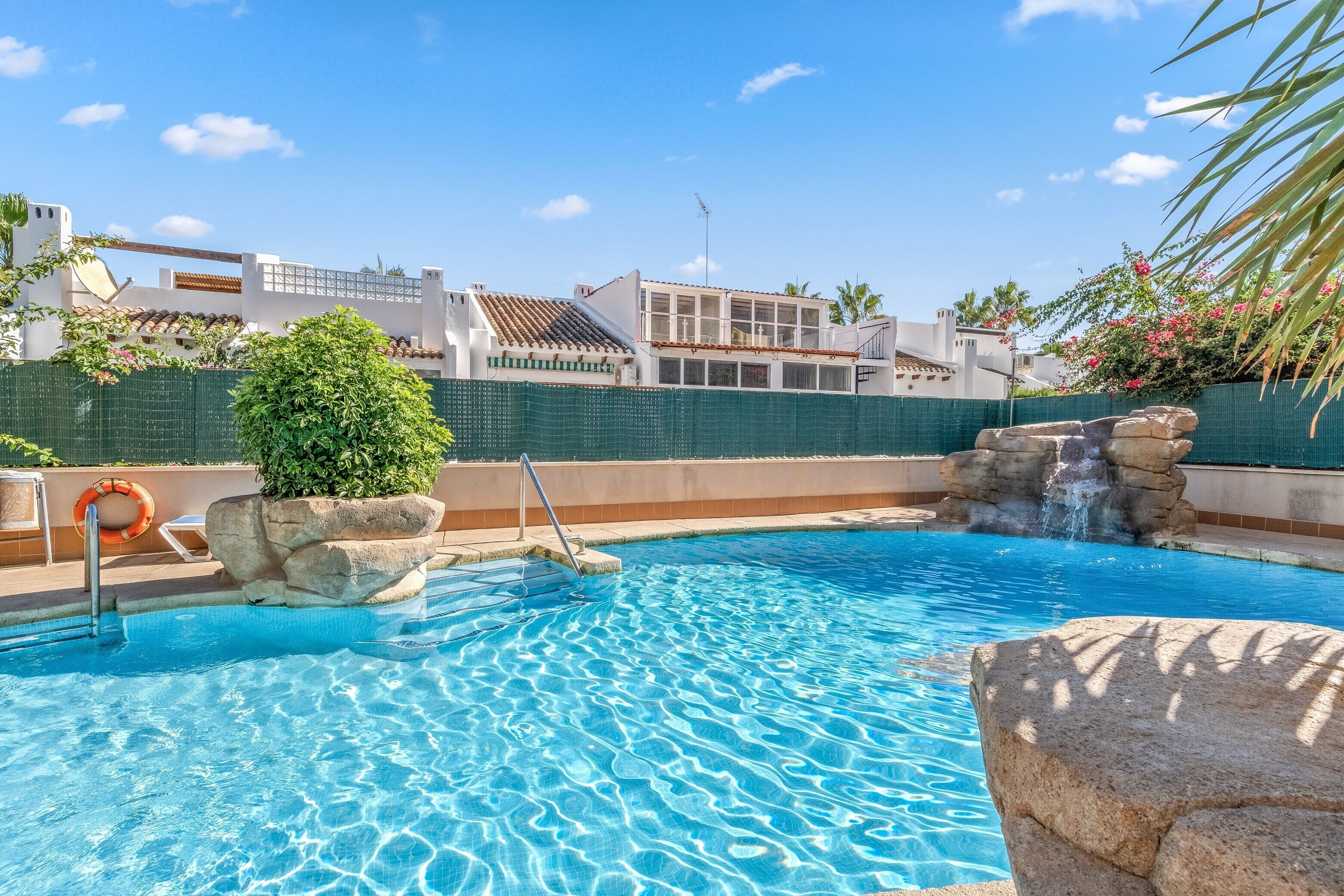 A swimming pool with clear blue water, a rock feature, and a lifebuoy.