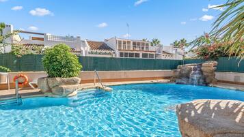 A swimming pool with clear blue water, a rock feature, and a lifebuoy.