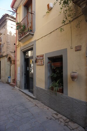 A building with a storefront, a balcony with plants, a door, and a window with a potted plant.
