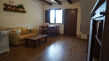 A living room with a sofa, coffee table, wooden flooring, a dining area with chairs, a window, and a door.