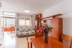 Un comedor con mesa de madera, sillas, un jarrón con flores y un sofá con una manta estampada.