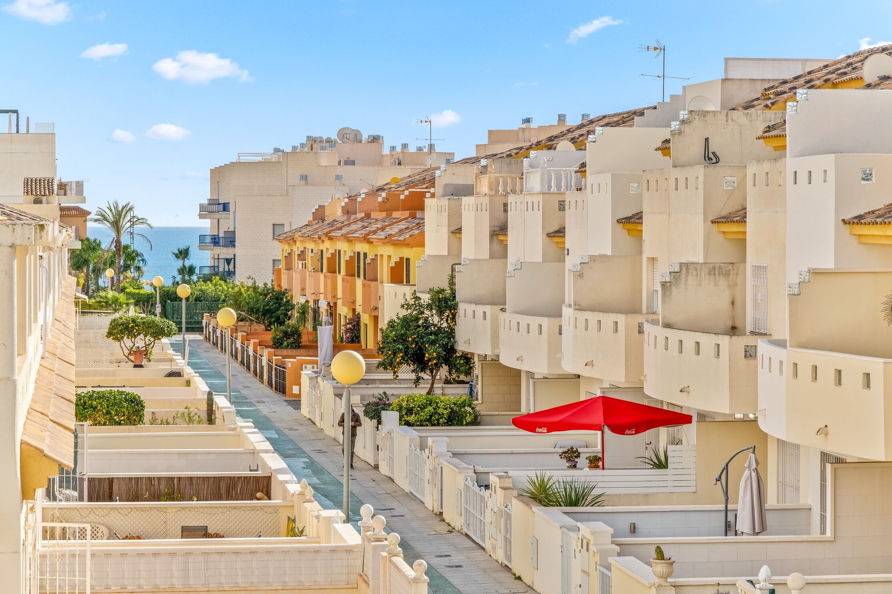 Una hilera de edificios modernos con balcones, una sombrilla roja y una vista despejada del mar.