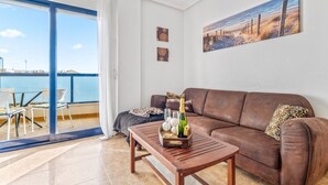 Uma sala de estar com um sofá de couro marrom, uma mesa de centro de madeira com uma garrafa e copos, e uma pintura de uma praia.