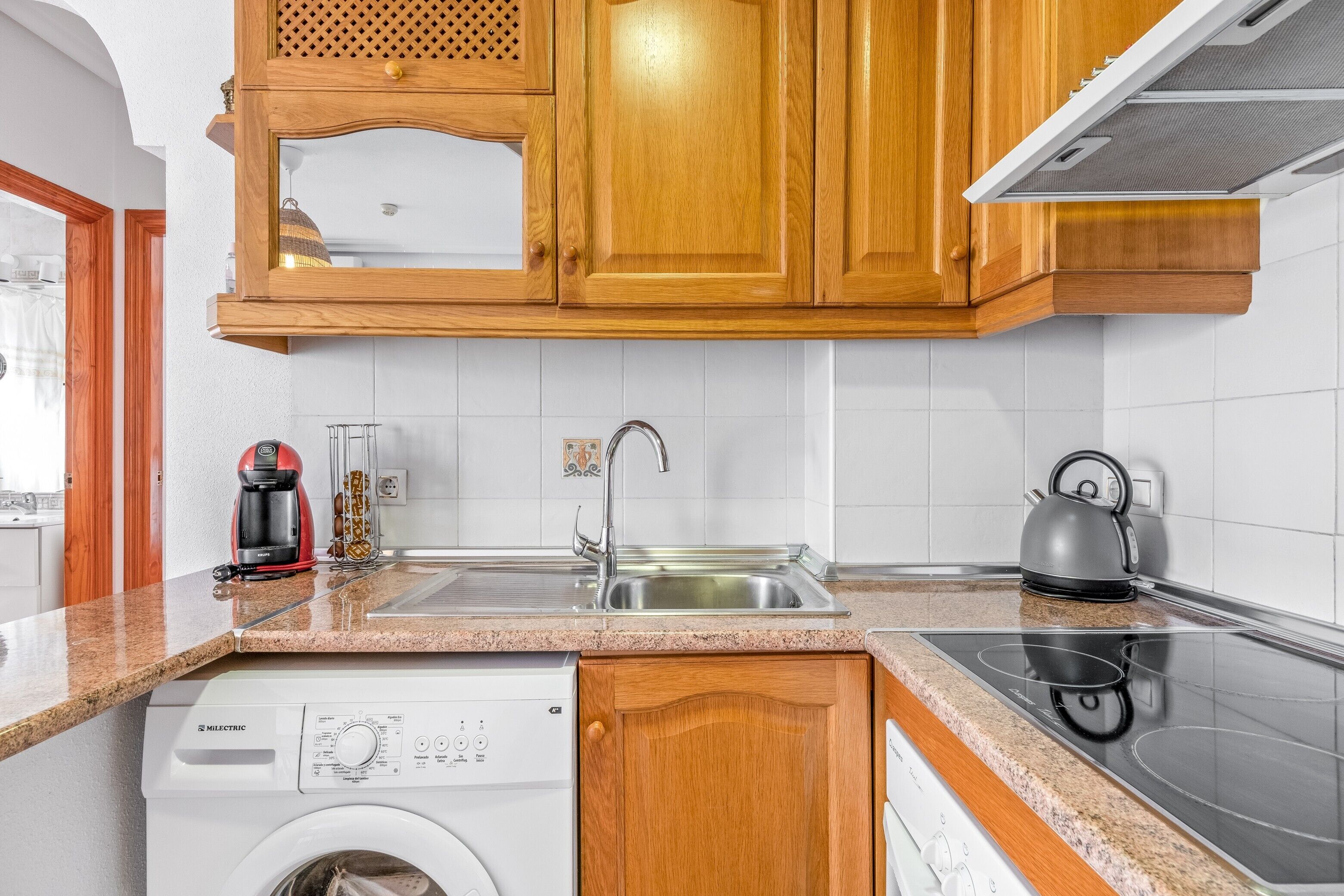 Una cucina con mobili in legno, lavatrice, macchina da caffè e bollitore.