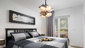 A modern bedroom with a large bed, a decorative light fixture, a framed artwork, and a balcony with a table and chairs.