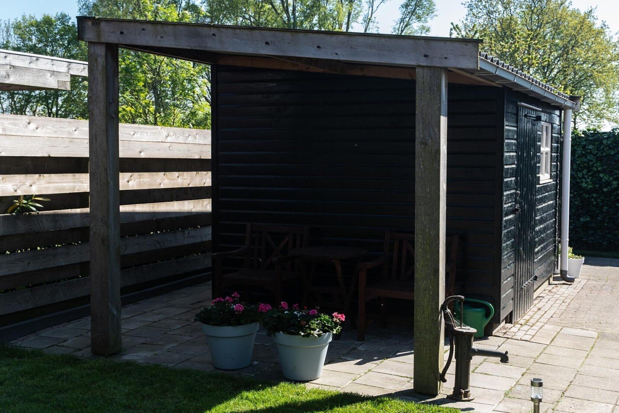 En træpergola med overdækket terrasse, plantekasser og udendørs møbler.