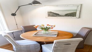 Une table de salle à manger ronde en bois, sur laquelle est posé un vase de fleurs, entourée de quatre chaises rembourrées.