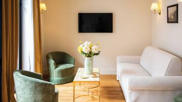 A living room with a sofa, two armchairs, a coffee table, a vase with flowers, a flat-screen TV, and wall-mounted lamps.