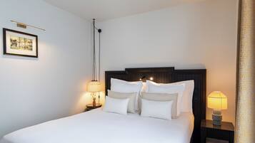 Un lit bien fait, avec du linge de lit blanc et plusieurs oreillers, une table de chevet avec une lampe et un tableau encadré au mur.