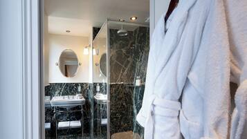 Een moderne badkamer met een douche in een glazen cabine, twee wastafels, een marmeren spatwand en een badjas aan een haak.