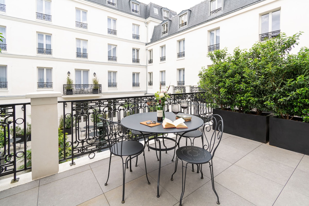 A round table with four chairs on a balcony, surrounded by a black wrought iron railing.
