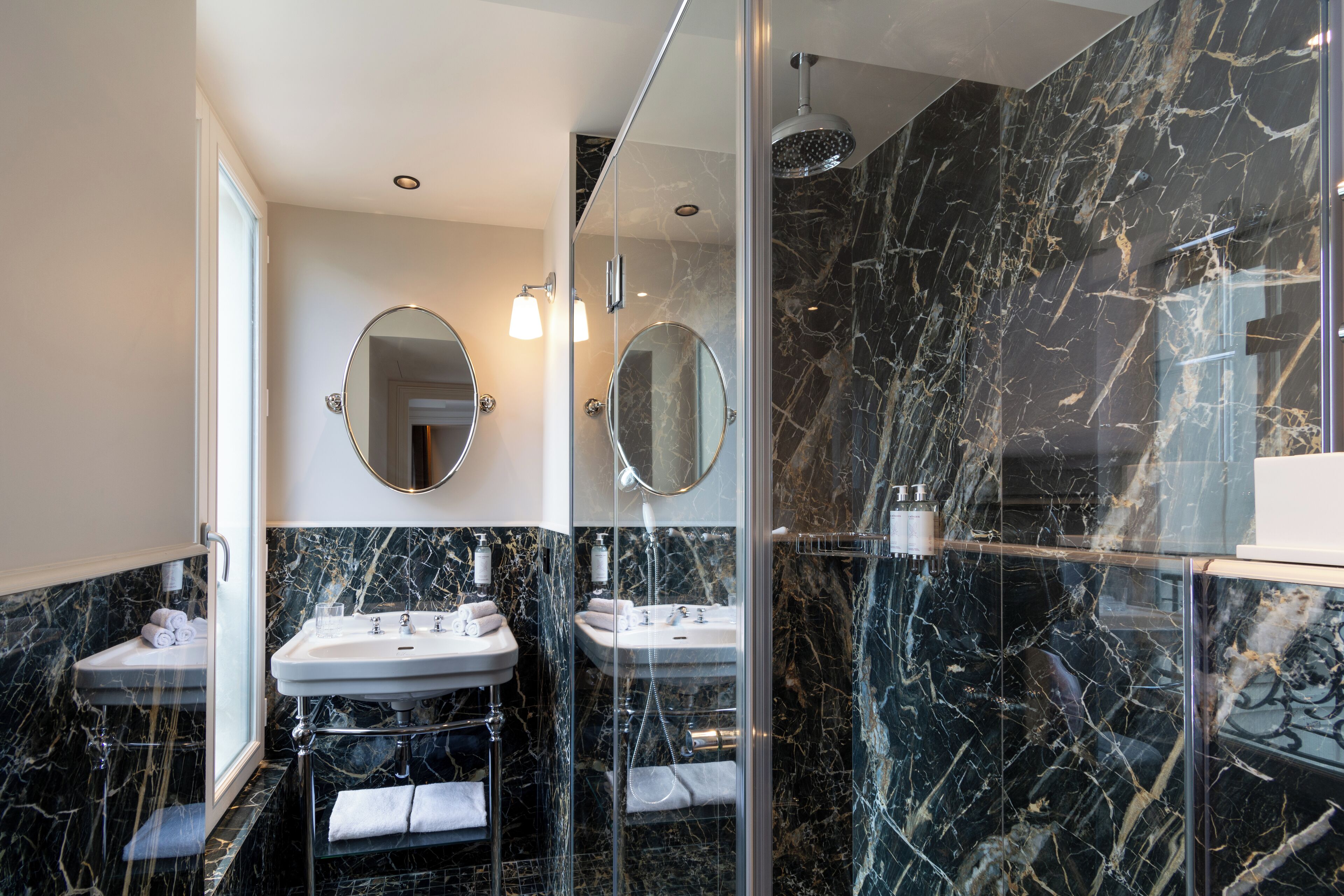 Un baño moderno con dos lavamanos, cabina de ducha de vidrio y paredes de mármol.
