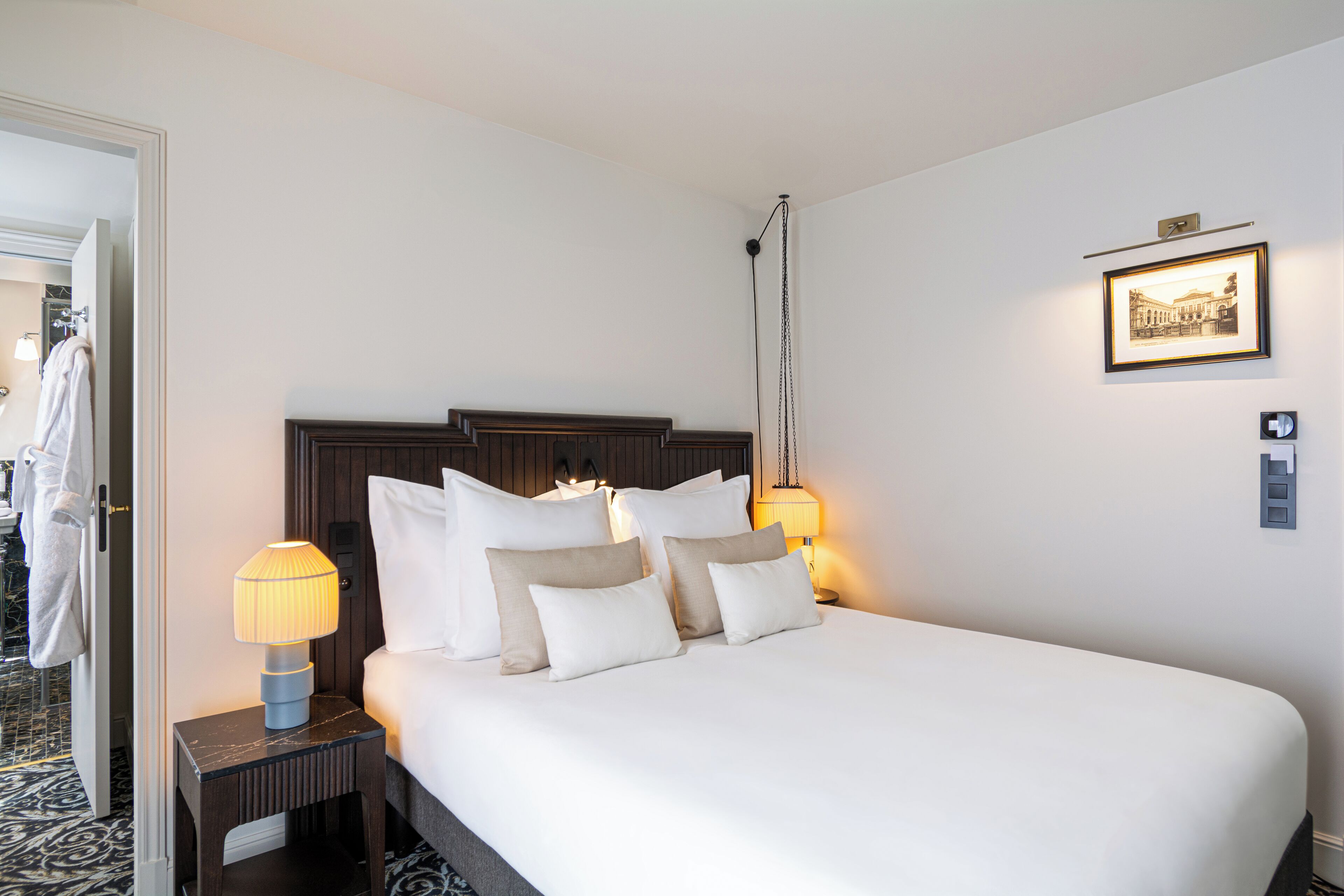 A hotel room with a large bed, two bedside lamps, a framed picture on the wall, and a door leading to a bathroom.