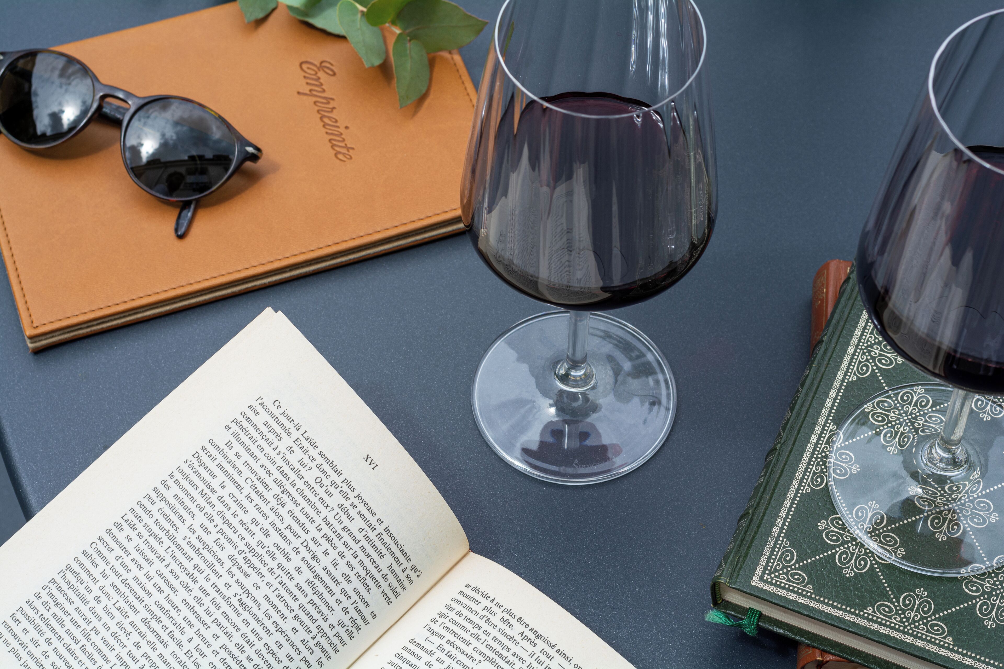 An open book, a pair of sunglasses, and two wine glasses on a table.