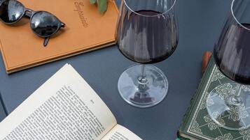 An open book, a pair of sunglasses, and two wine glasses on a table.