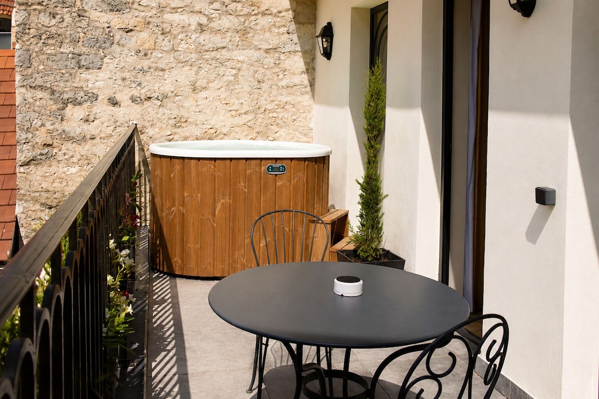 A patio with a round table and chairs, a wooden hot tub, and a stone wall.