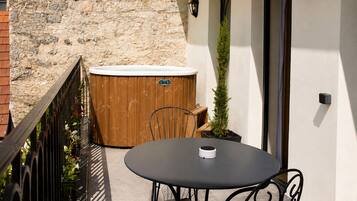 A patio with a round table and chairs, a wooden hot tub, and a stone wall.