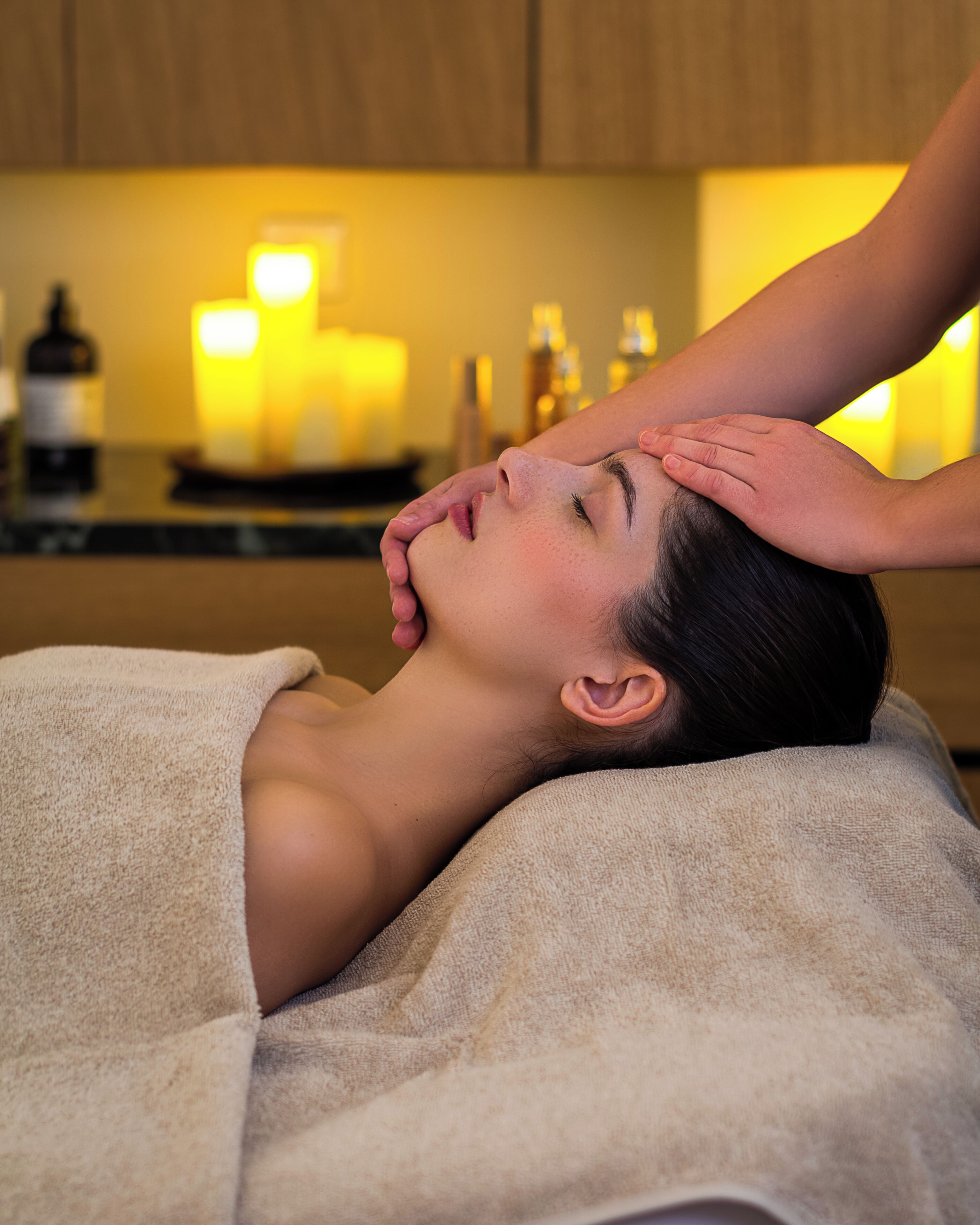 En person får massage i ett rum med ett träskåp och ljus i bakgrunden.