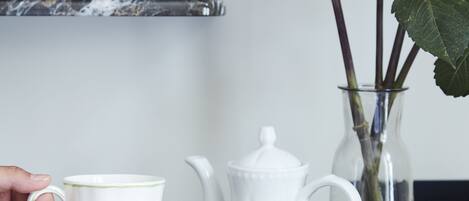 A white teapot, a white cup, a white plate, a vase with flowers, and a stack of books on a dark surface.