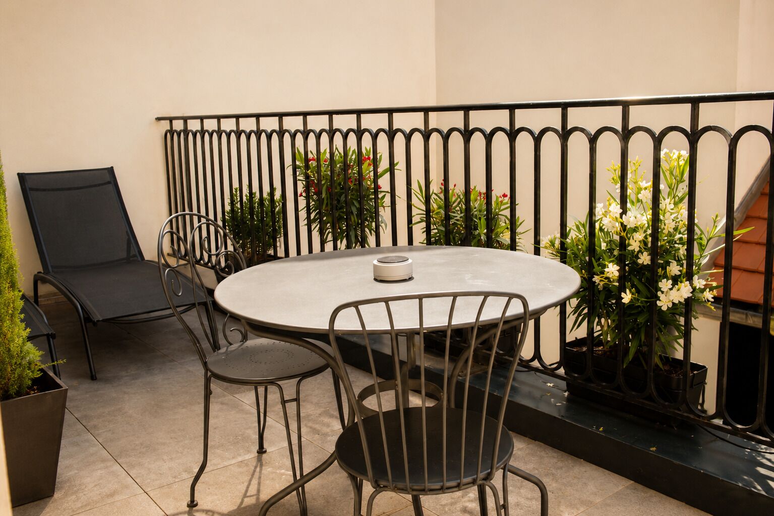 Una mesa metálica redonda con cuatro sillas, una mesa pequeña redonda y plantas en macetas en un balcón con baranda de metal.