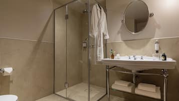 Un baño moderno con ducha de vidrio, un lavabo blanco con espejo y toallas ordenadas en un estante.