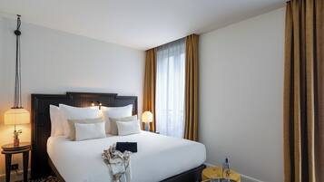 A hotel room with a large bed, two bedside lamps, a small table with a glass, and a nightstand with a lamp.