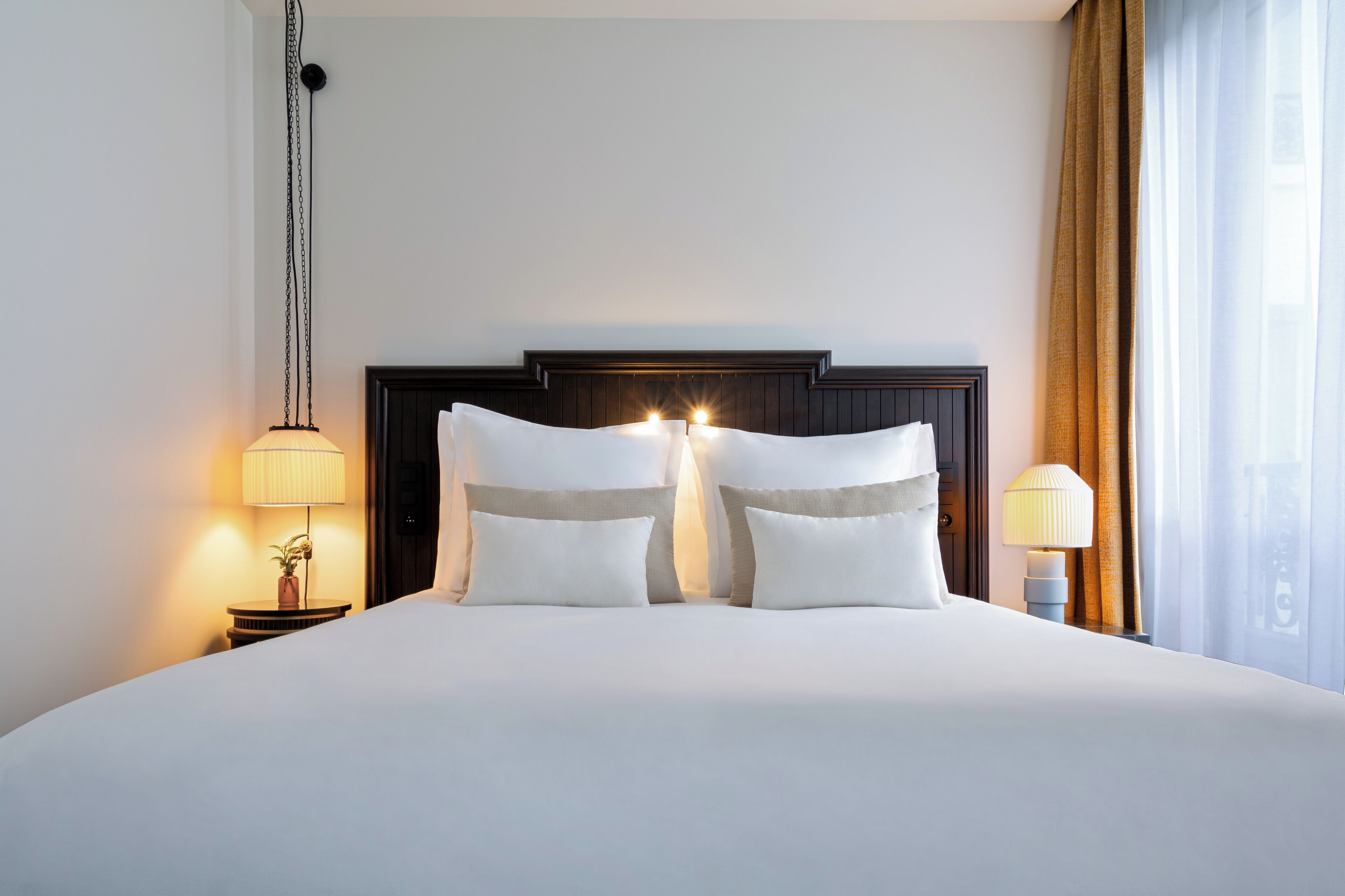 A hotel room with a large bed, two bedside tables, a nightstand, a lamp, and a window with curtains.