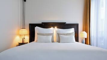 A hotel room with a large bed, two bedside tables, a nightstand, a lamp, and a window with curtains.