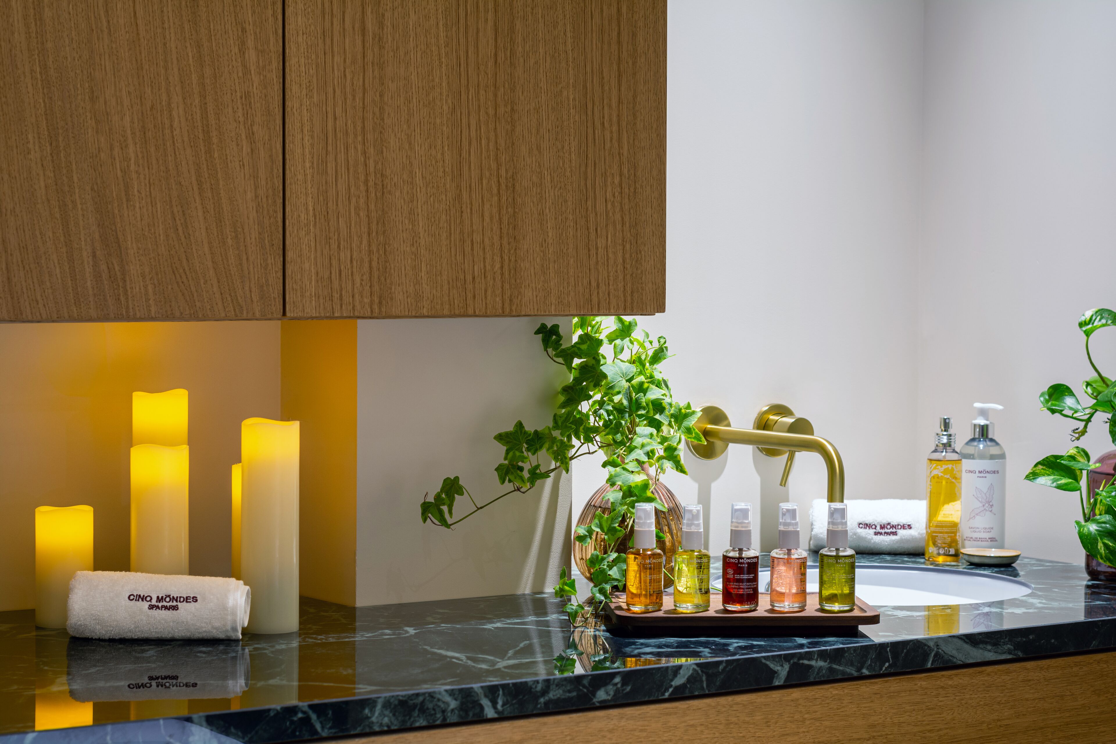 A bathroom with a marble countertop, a sink, and a mirror. There are candles, a towel, and a plant on the counter.