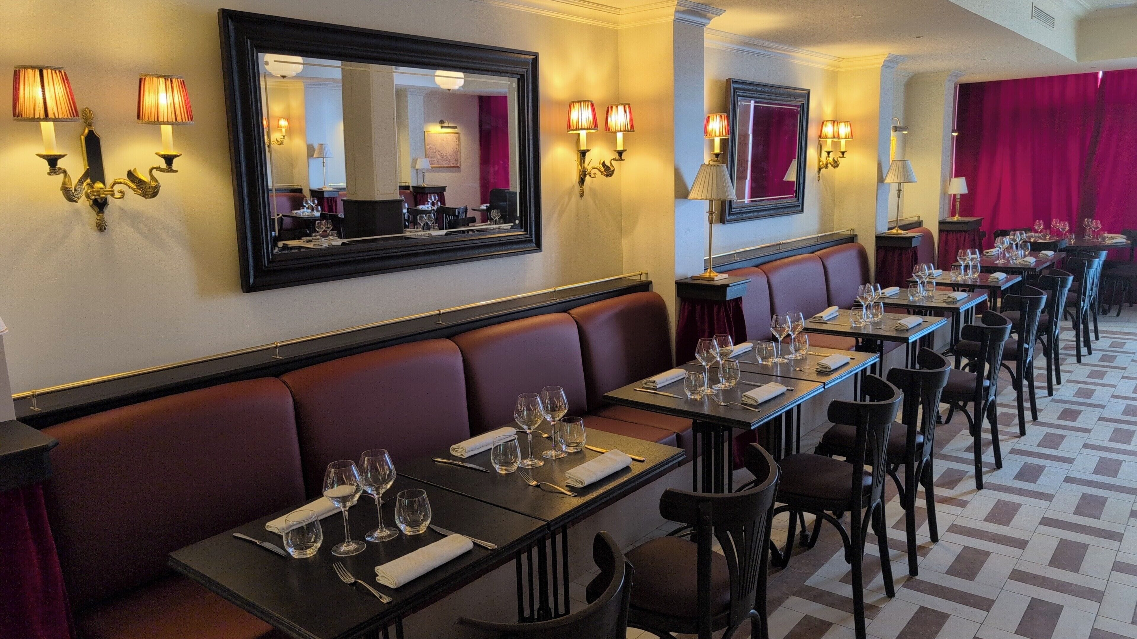 Un restaurant avec des tables dressées, un grand miroir et des appliques murales.