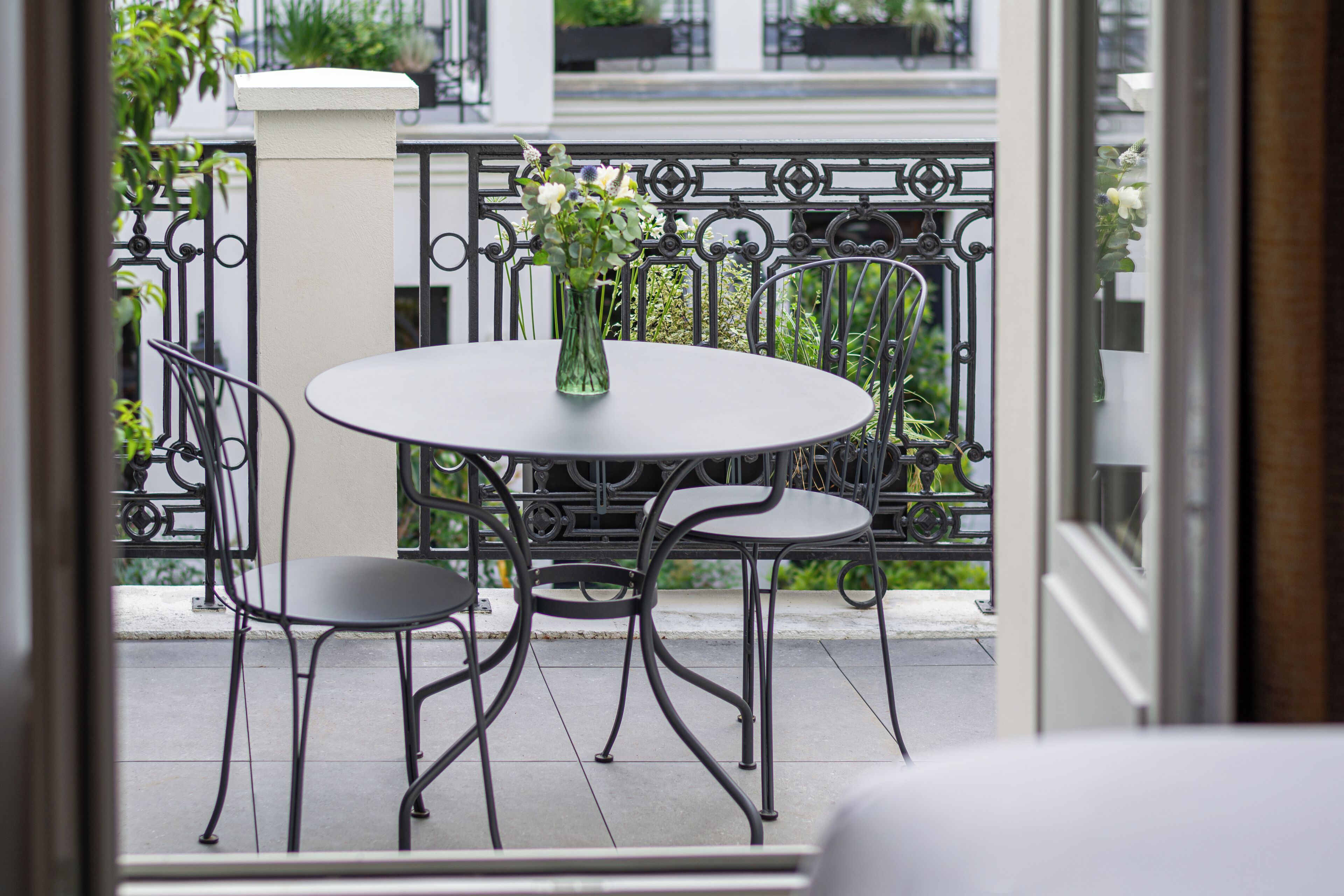 Ein Balkon mit rundem Tisch, zwei Stühlen, einer Blumenvase und einer weißen Säule.