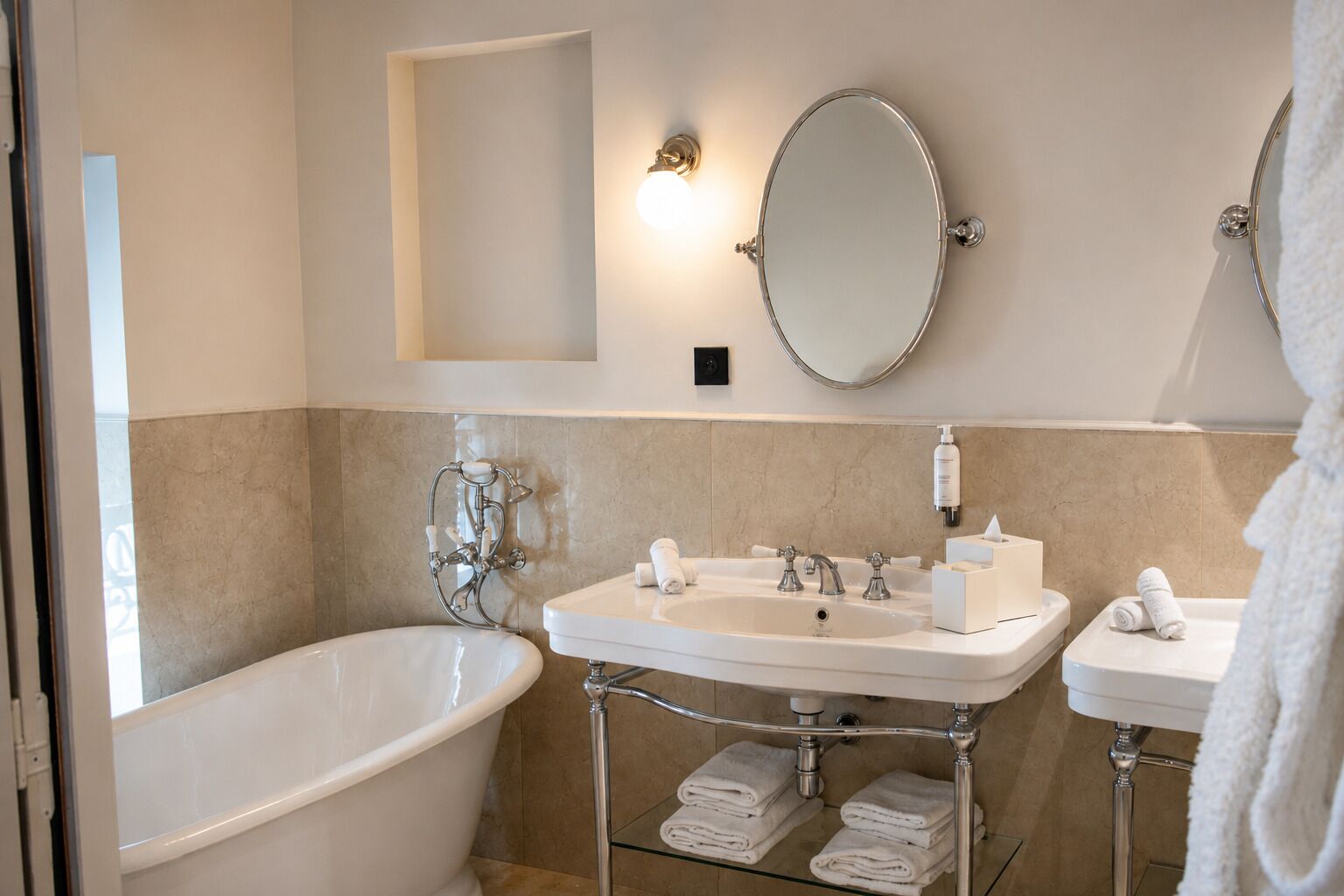 Un baño con bañera, dos lavamanos, un espejo y un perchero para toallas.