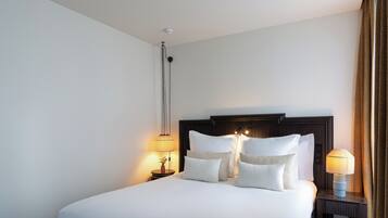 A neatly made bed with white linens and multiple pillows, a dark wooden headboard, a bedside lamp, and a wall-mounted light fixture.