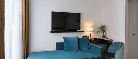A hotel room with a bed, a TV mounted on the wall, a bedside table with a lamp, and a chair.