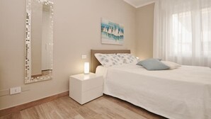 A bedroom with a bed, a nightstand, a mirror, and a painting on the wall.