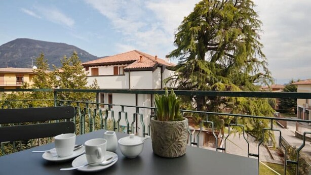 A balcony with a table set for two, a potted plant, and a view of a mountain and houses in the background.