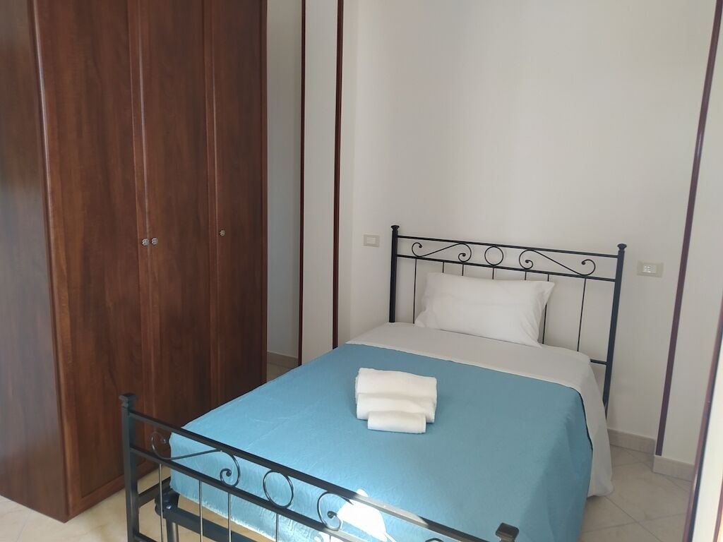 Uma cama de solteiro com estrutura de metal, uma colcha azul e travesseiros brancos.